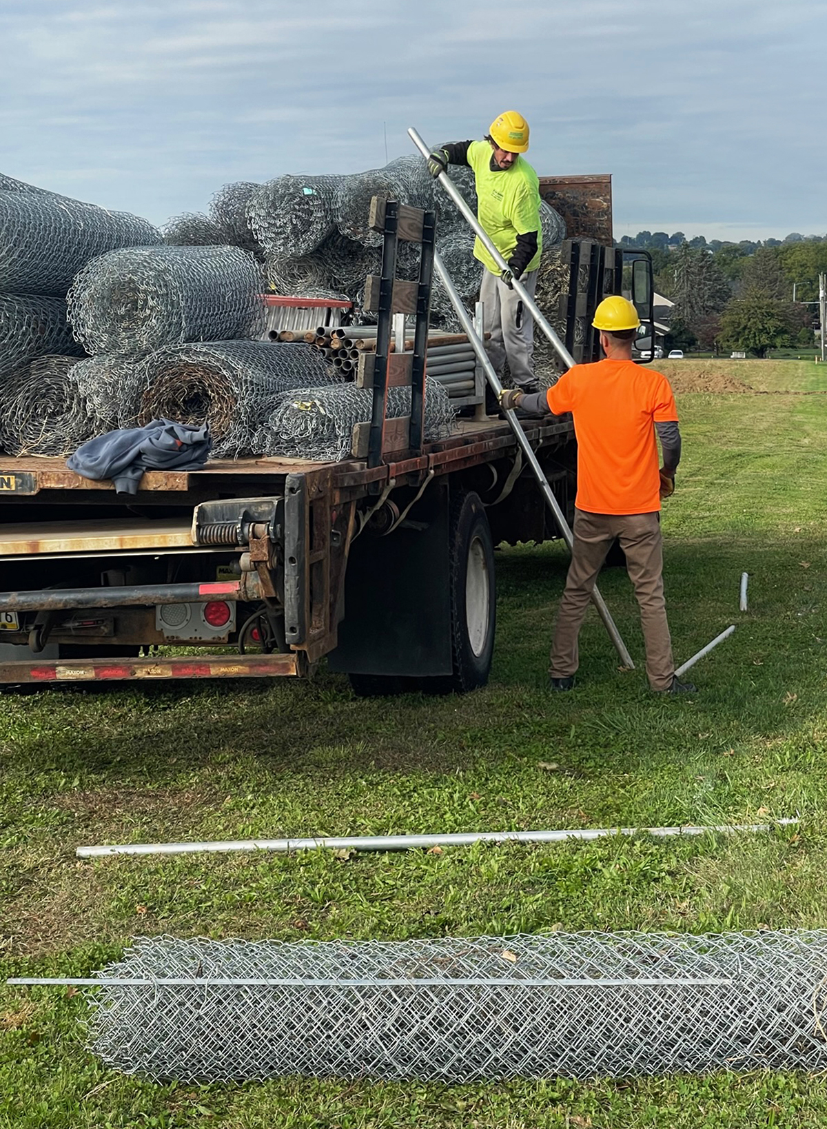 two workers unloading rolls of chain link fence from truck
